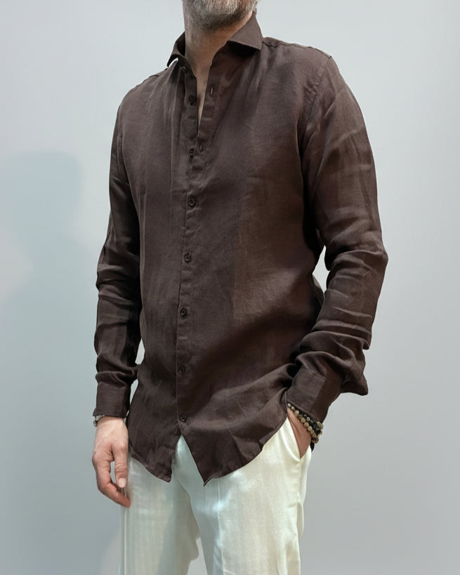 Model wearing a brown button-up shirt and white pants against light grey backdrop