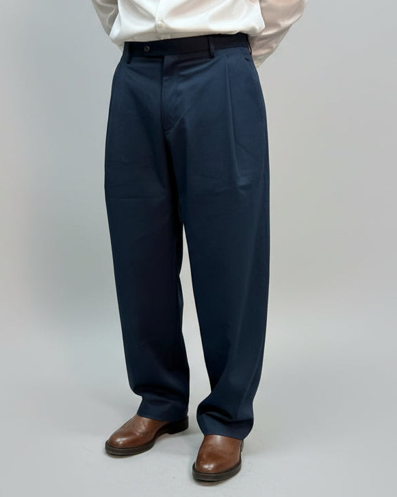 Person wearing white shirt, navy pants and brown shoes in front of a light grey curtain.