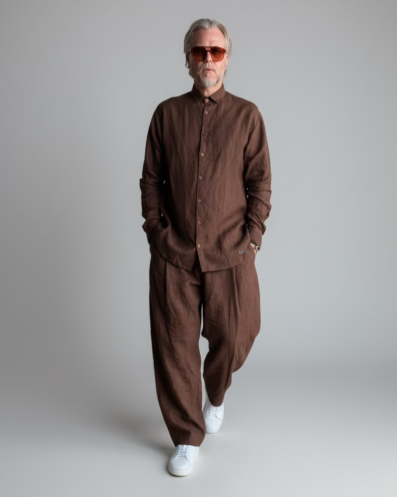 Man in a brown outfit standing against light grey backdrop
