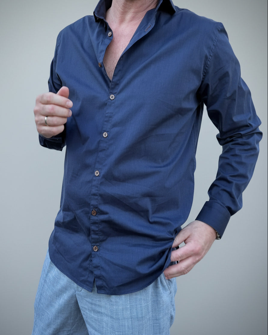 Person wearing a navy blue button-up shirt in front of light grey backdop