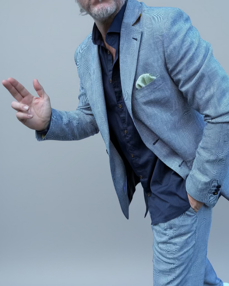 Man in a gray, blue checked suit standing in front of a light grey backdrop.