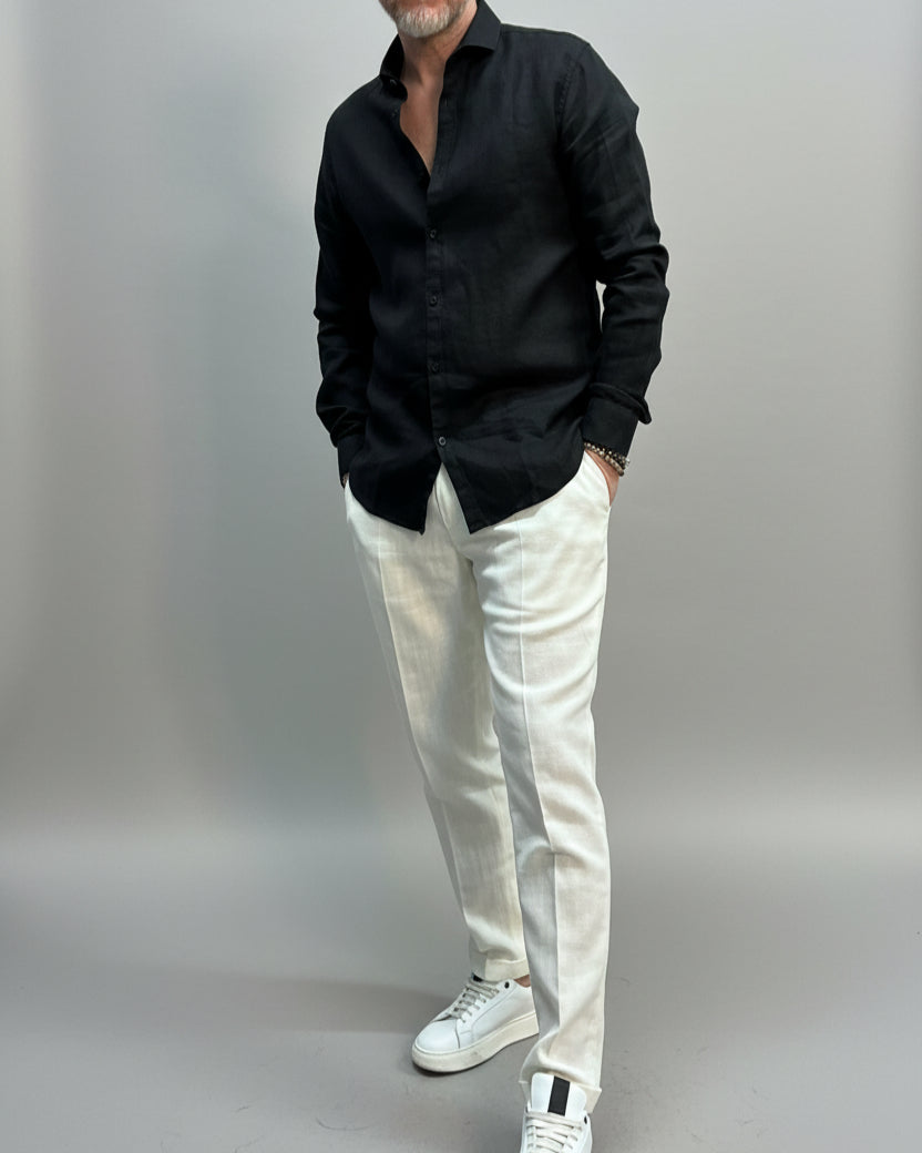 Model wearing a black shirt and white pants in front of light grey backdrop