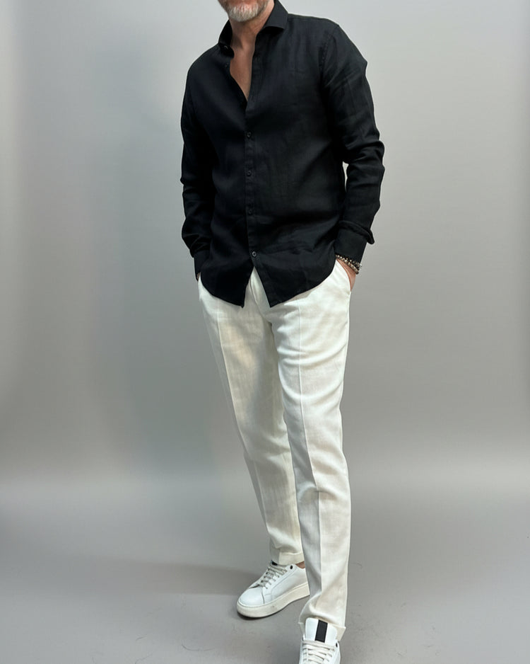 Model wearing a black shirt and white pants in front of light grey backdrop