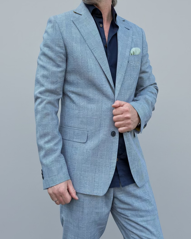 Man in a gray, blue checked suit standing in front of a light grey backdrop.