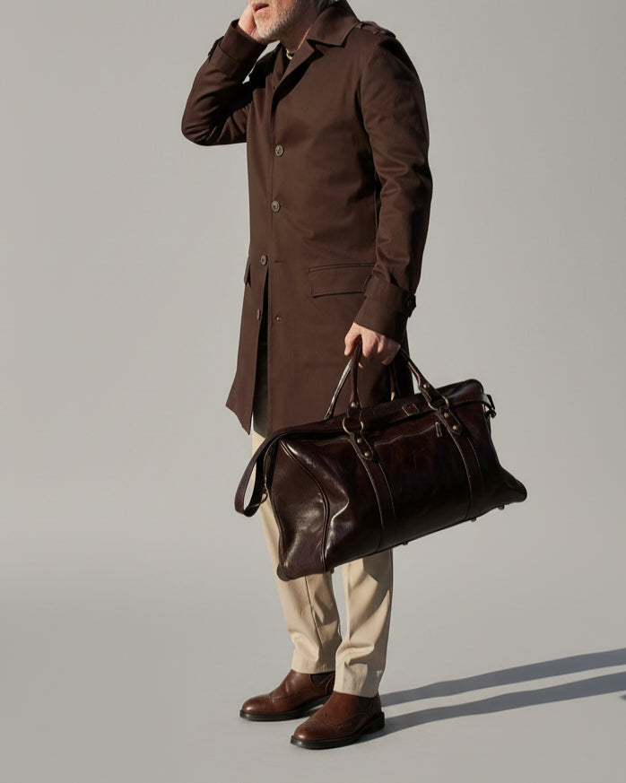 MODEL STANDING IN FRONT OF L. GREY BACKDROP WEARING A BROWN TRENCH COAT