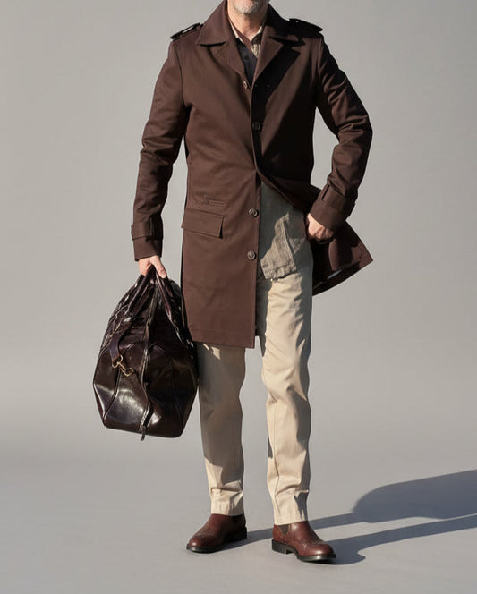 MODEL STANDING IN FRONT OF L. GREY BACKDROP WEARING A BROWN TRENCH COAT