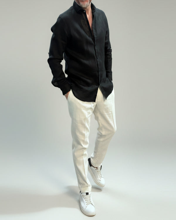 Model wearing a black linen shirt and white pants on a plain background
