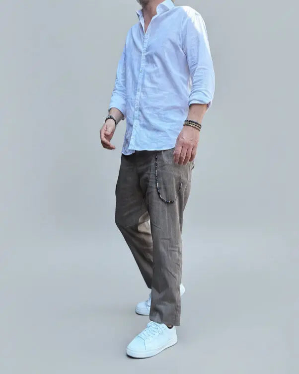 Model standing in front of light grey backdrop wearing brown linen pants and white shirt and sneakers