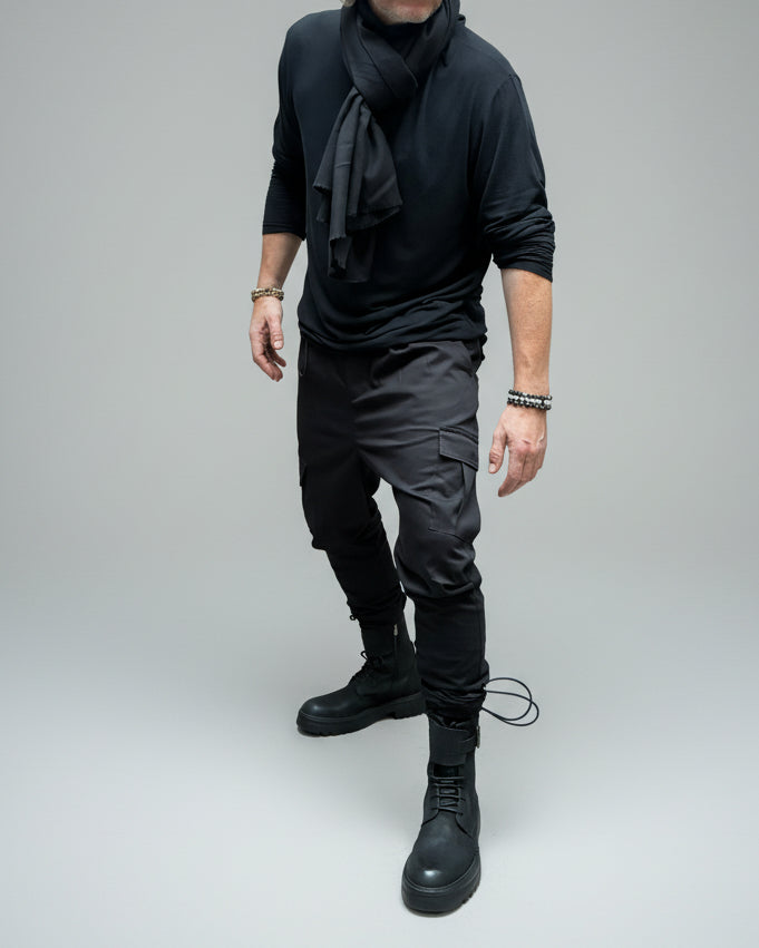 Person wearing a black outfit with boots standing on a pink platform. In a dynamic position