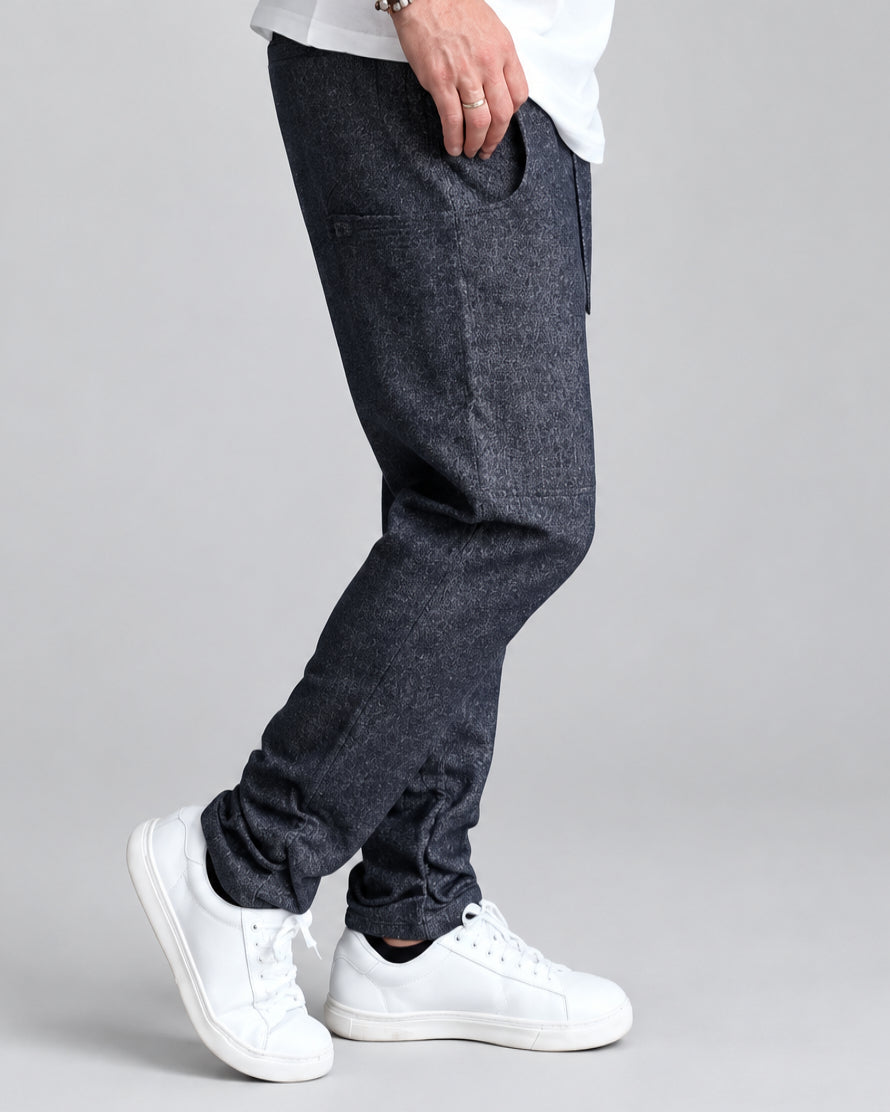 A person wearing navy blue melange jogger pants with side pockets, paired with white sneakers, standing against a white painted brick wall.