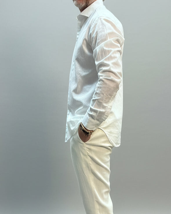 Model wearing a white linen shirt and white pants in front of light grey backdrop 