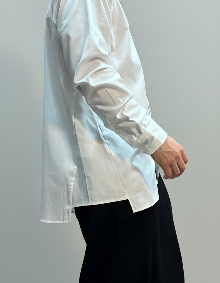 Person wearing a white shirt and black pants against a beige curtain background
