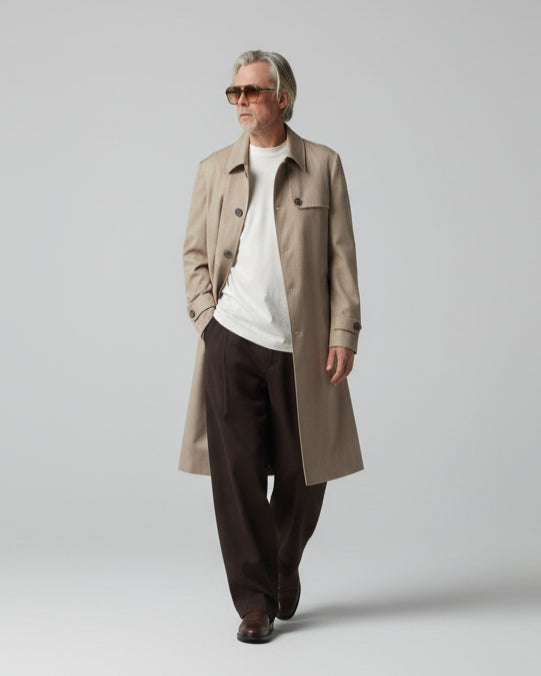 MODEL WEARING A BEIGE COAT IN FRONT OF A GREY BACKDROP
