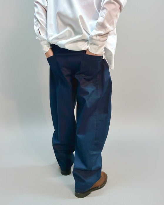 Person wearing a white shirt and blue pants standing backwards in front of light grey background.