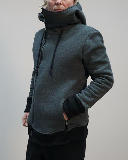 Person wearing a gray hoodie standing on a light grey surface with a blurred background