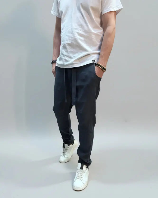 Person wearing a white T-shirt and blue pants standing on a gray floor with a brown fabric draped over them.