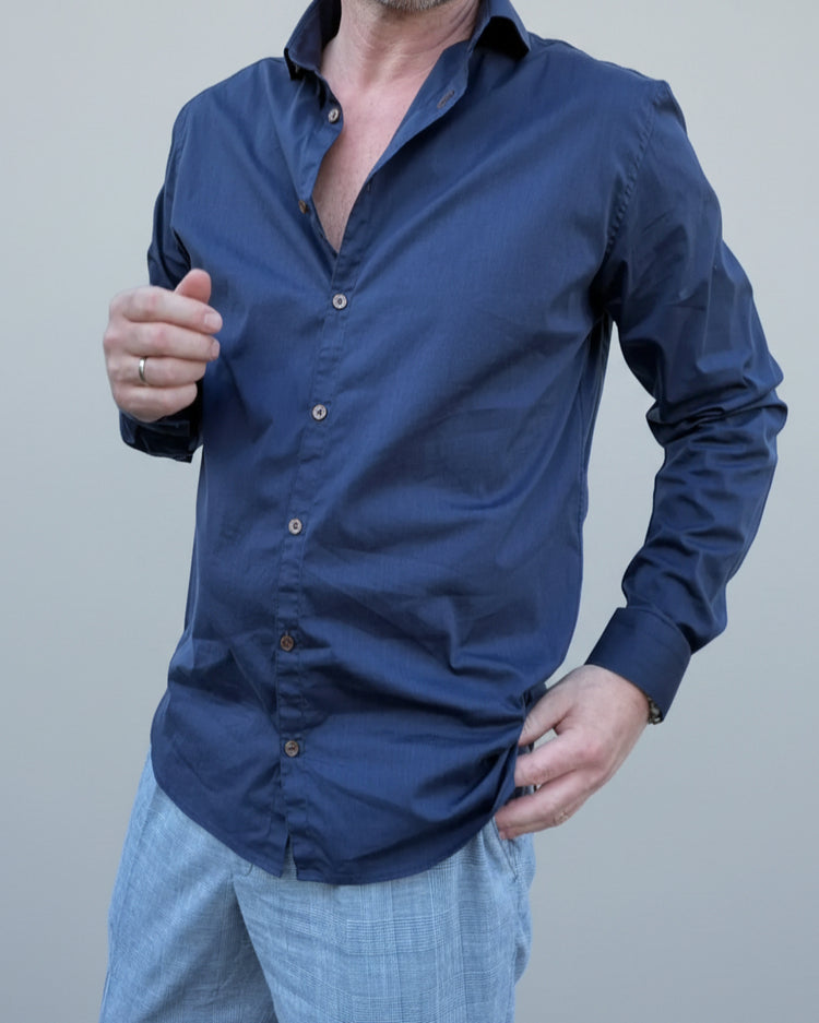Person wearing a navy blue button-up shirt in front of light grey backdop