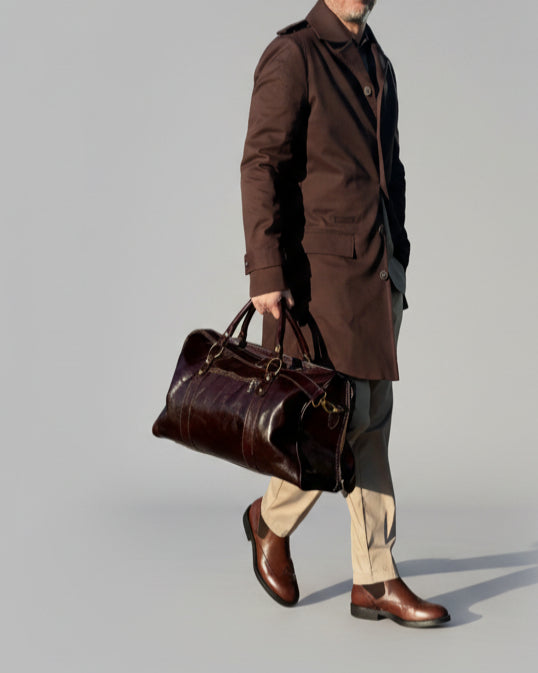 MODEL STANDING IN FRONT OF L. GREY BACKDROP WEARING A BROWN TRENCH COAT