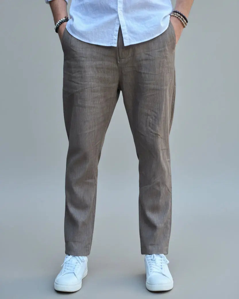 Model standing in front of light grey backdrop wearing brown linen pants and white shirt and sneakers