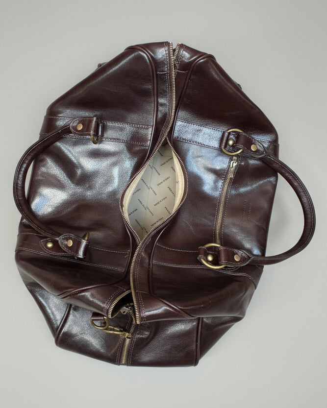 Brown leather bag with gold hardware and leather shoulder strap on a light pink background
