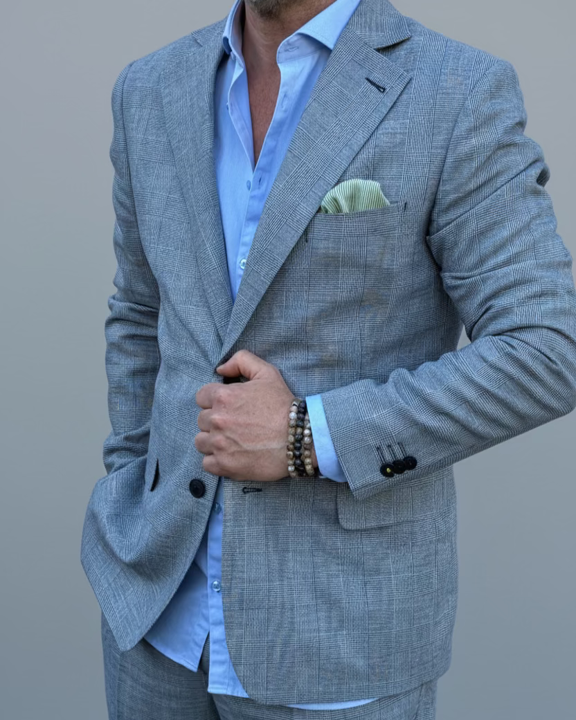 Man in a gray, blue checked suit standing in front of a light grey backdrop.