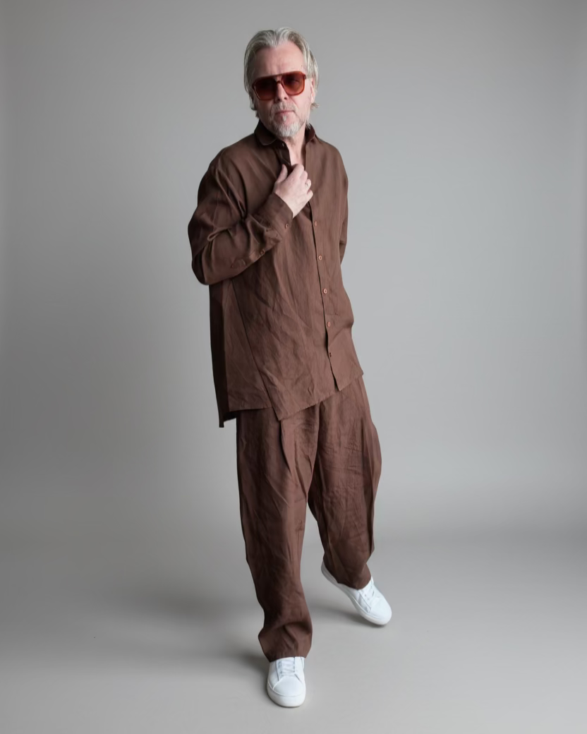 Man in a brown outfit standing against light grey backdrop