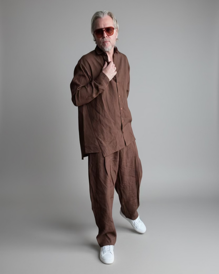 Man in a brown outfit standing against light grey backdrop