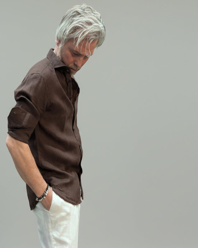 Model wearing a brown button-up shirt and white pants against light grey backdrop