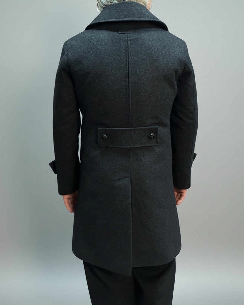 Person wearing a Grey coat standing on a beige mat with a blurred background