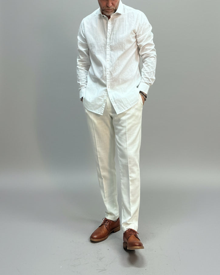 Model wearing a white linen shirt and pants in front of light grey backdrop 