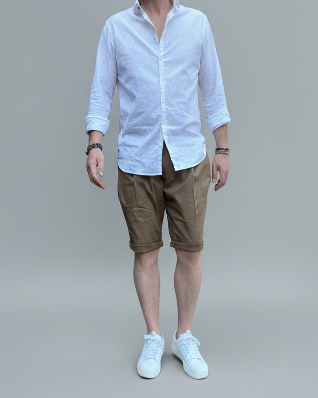 Person wearing a white shirt, brown shorts, and white sneakers in front of light grey backdrop.