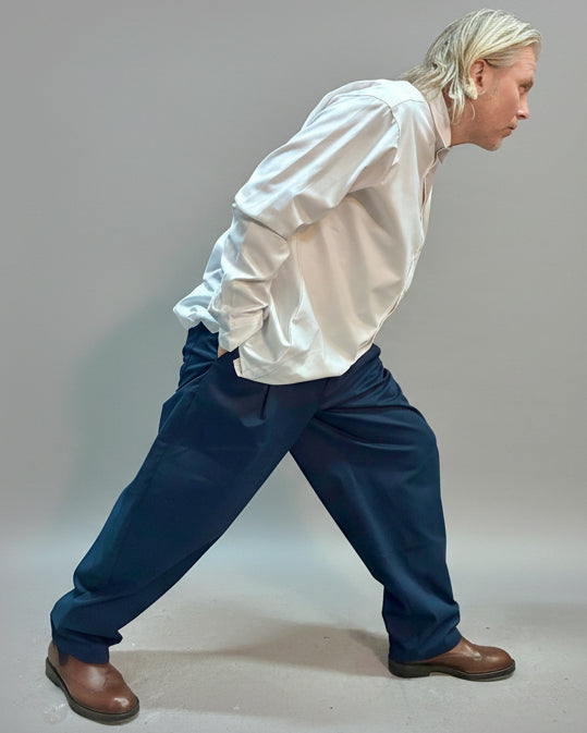 Person wearing a white shirt and blue pants in front of light grey backdrop.