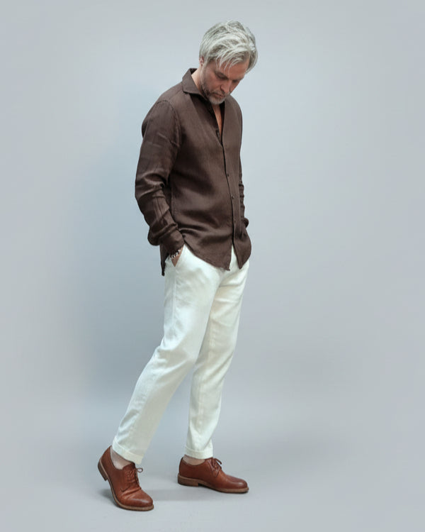 Model wearing a brown button-up shirt and white pants against light grey backdrop
