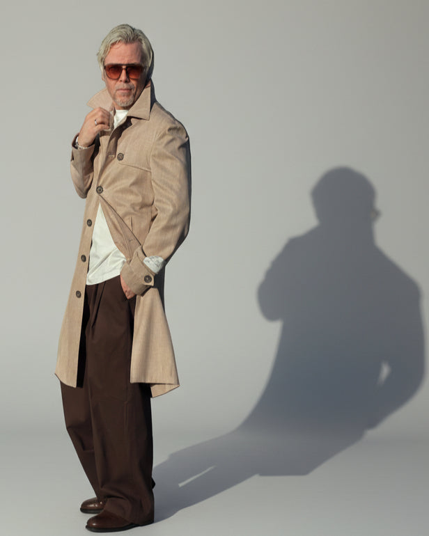MODEL WEARING A BEIGE COAT IN FRONT OF A GREY BACKDROP