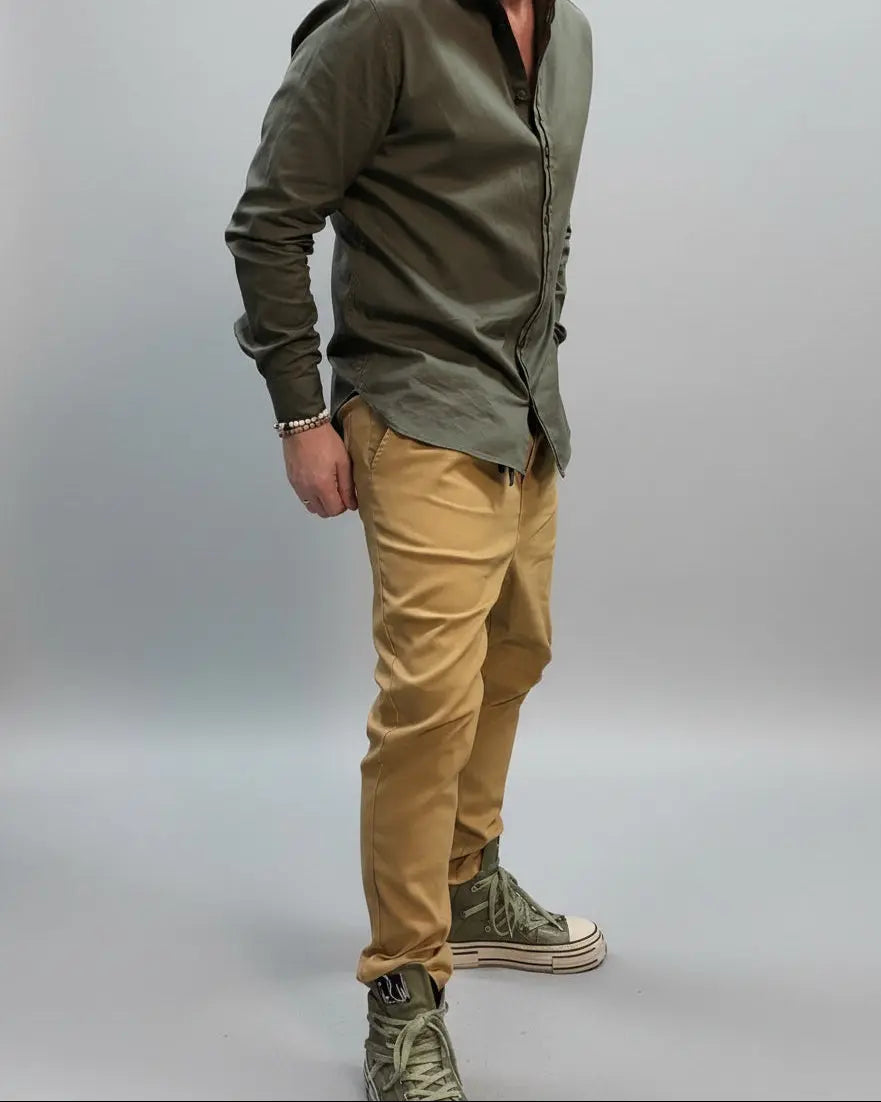 Model in a dynamic position wearing a green shirt and beige pants in a minimal indoor setting