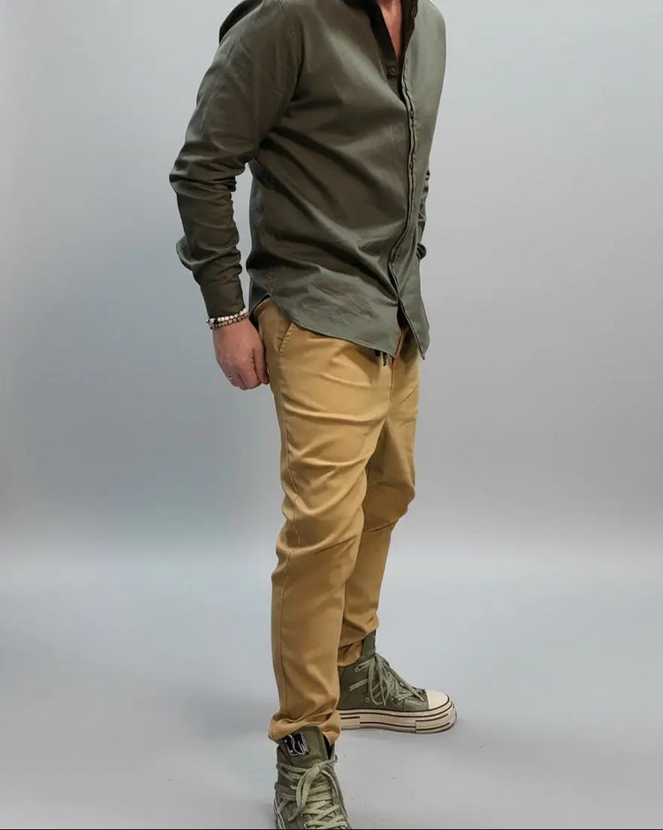 Model in a dynamic position wearing a green shirt and beige pants in a minimal indoor setting