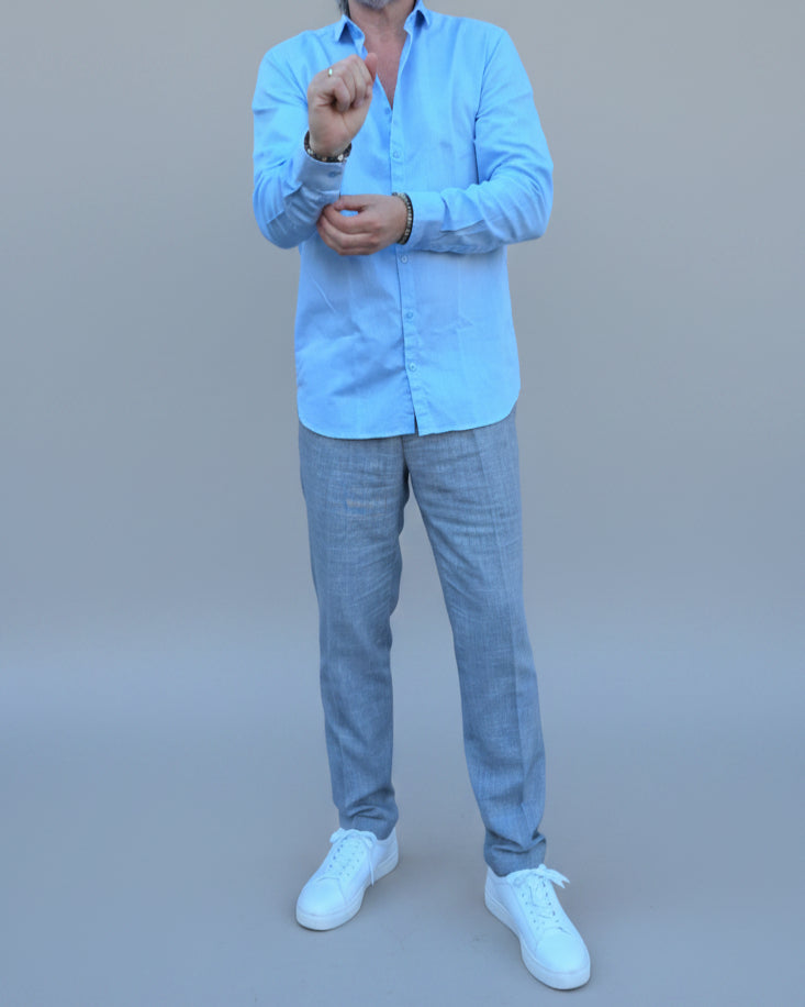 Man in light blue shirt and gray pants standing in front of light grey backdrop