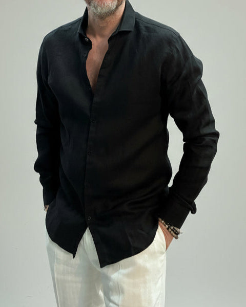 Model wearing a black linen shirt and white pants on a plain background
