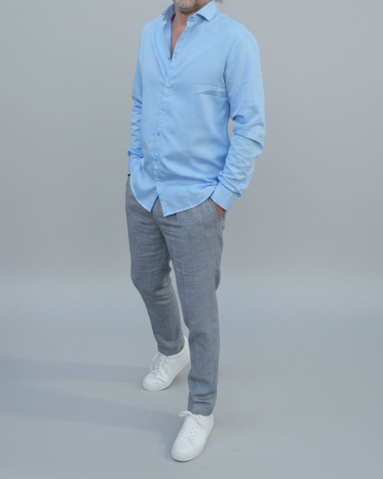 Man in light blue shirt and gray pants standing in front of light grey backdrop
