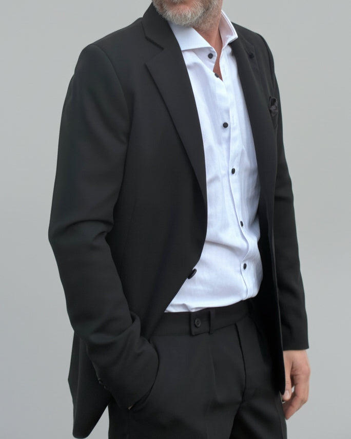 Model standing in front of light grey backdrop wearing black suit and white shirt.