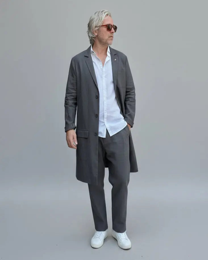 Person wearing a white shirt, gray linen pants, and white sneakers on a light grey background in a dynamic possition.