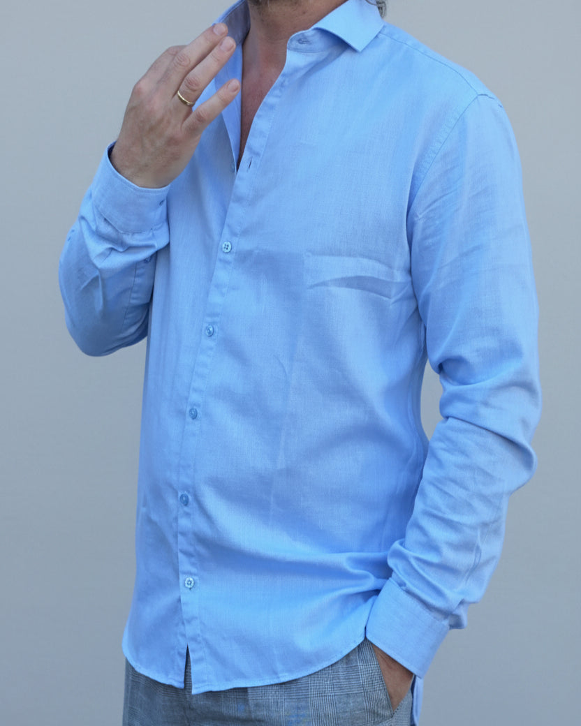 Man in light blue shirt and gray pants standing in front of light grey backdrop