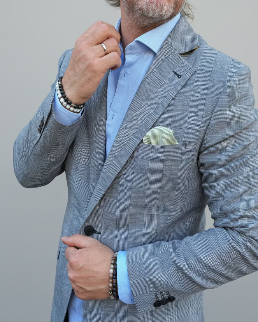 Man in a gray, blue checked suit standing in front of a light grey backdrop.