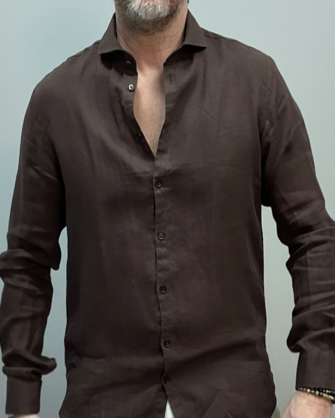 Model wearing a brown button-up shirt and white pants against light grey backdrop