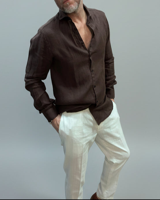 Model wearing a brown button-up shirt and white pants against light grey backdrop