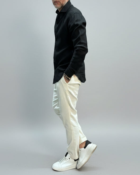 Model wearing a black linen shirt and white pants on a plain background