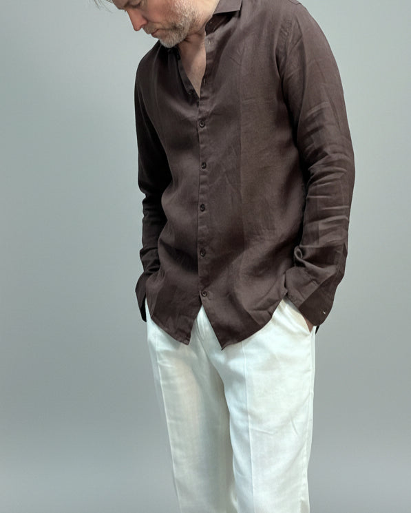 Model wearing a brown button-up shirt and white pants against light grey backdrop