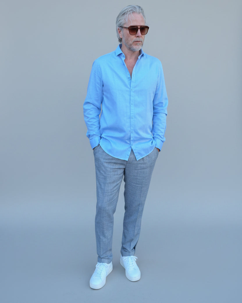 Man in light blue shirt and gray pants standing in front of light grey backdrop