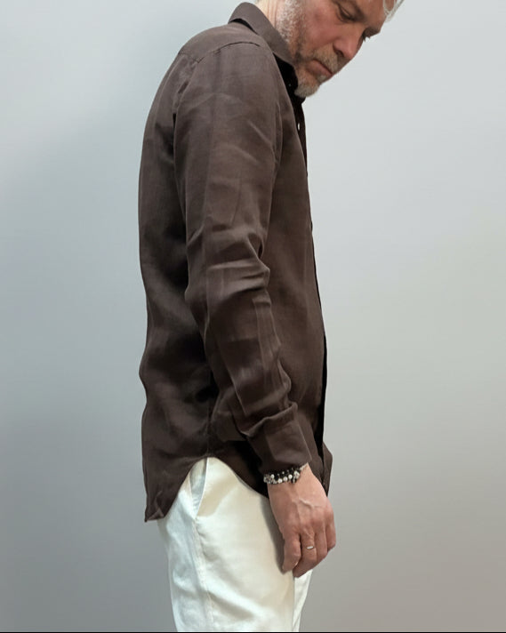 Model wearing a brown button-up shirt and white pants against light grey backdrop