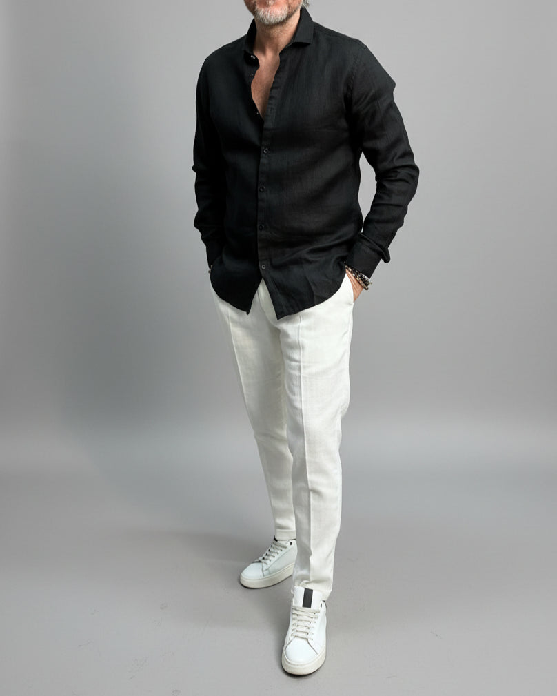 Model wearing a black linen shirt and white pants on a plain background